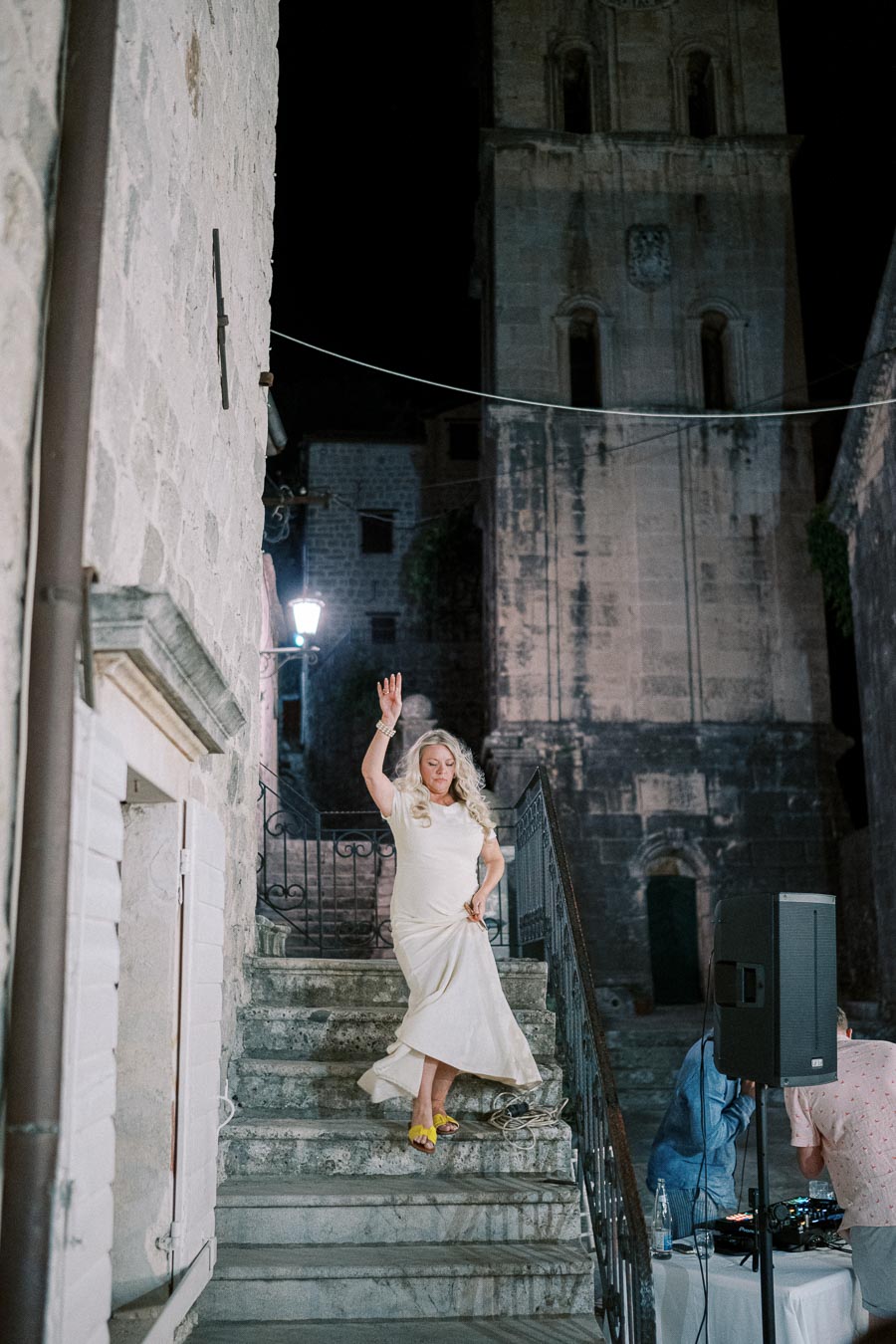 Woman in a white dress dancing on stone steps at night, with an ancient stone building in the background.