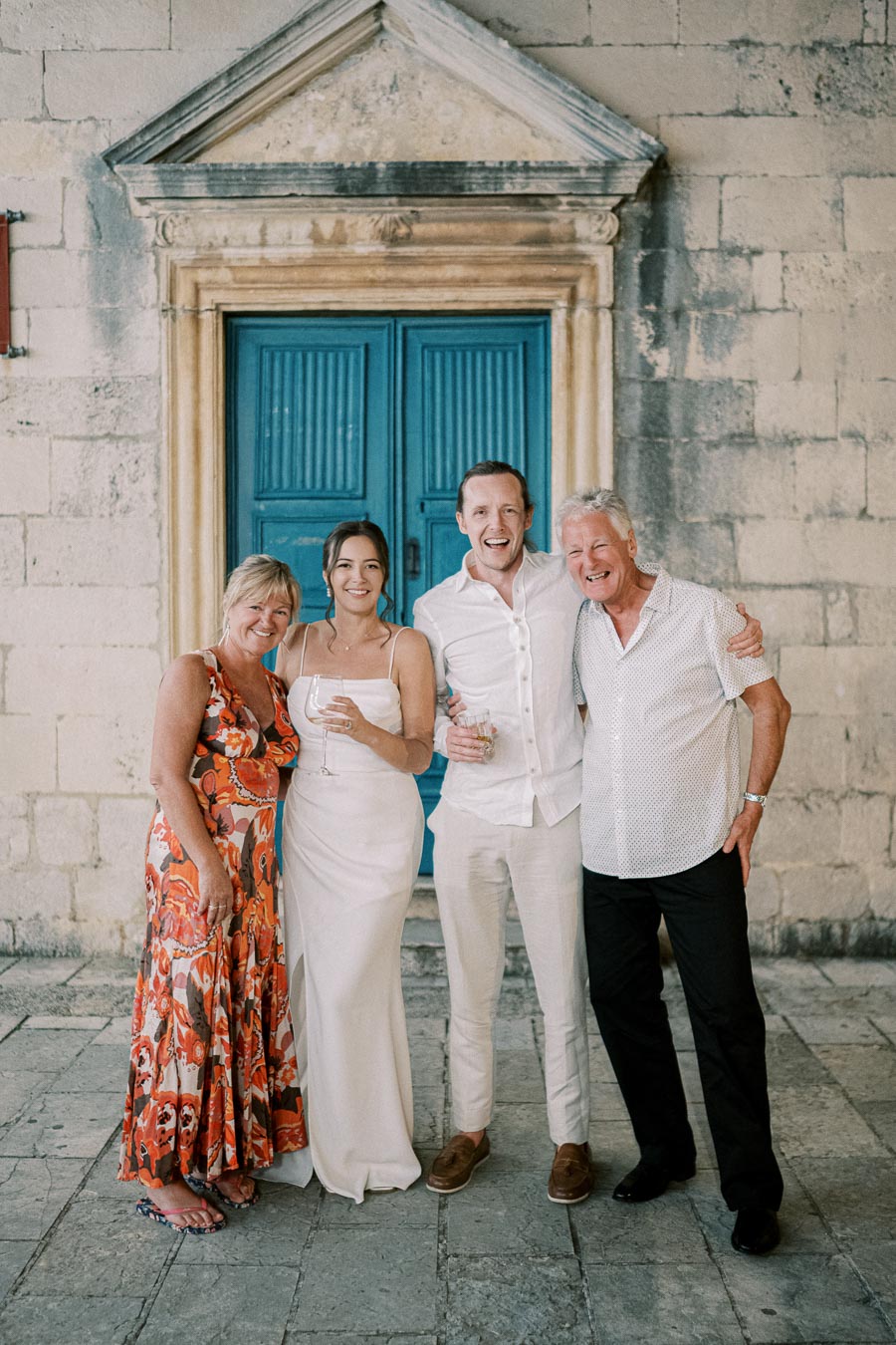 A group of four people smiling and posing in front of a rustic building with a vibrant blue door.