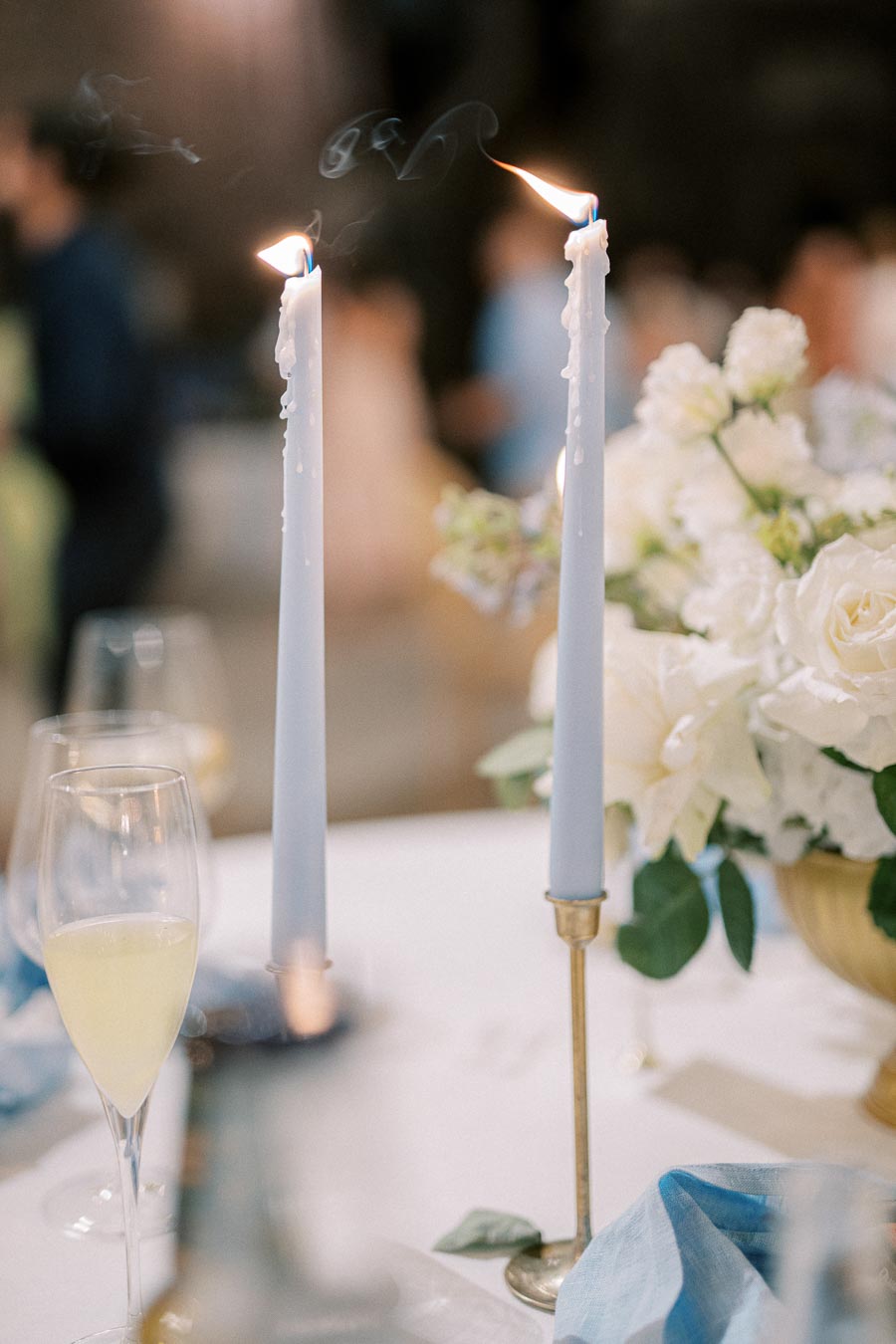 Elegant wedding table setting with lit blue taper candles, a floral centerpiece with white roses, and a champagne glass, creating a romantic ambiance.