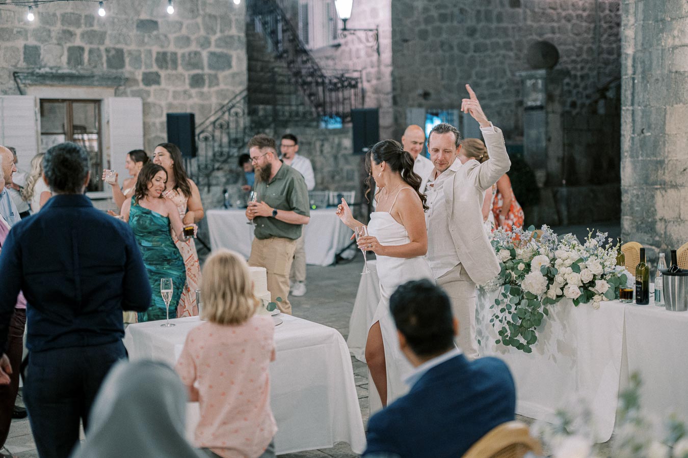 Guests enjoying a vibrant wedding reception with dancing and celebration in a rustic stone venue, featuring elegant floral decorations and twinkling lights.
