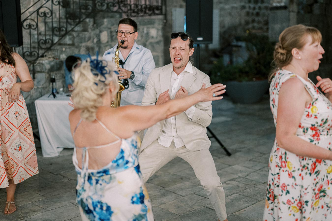 Group of people dancing energetically at an outdoor event with a saxophone player in the background.