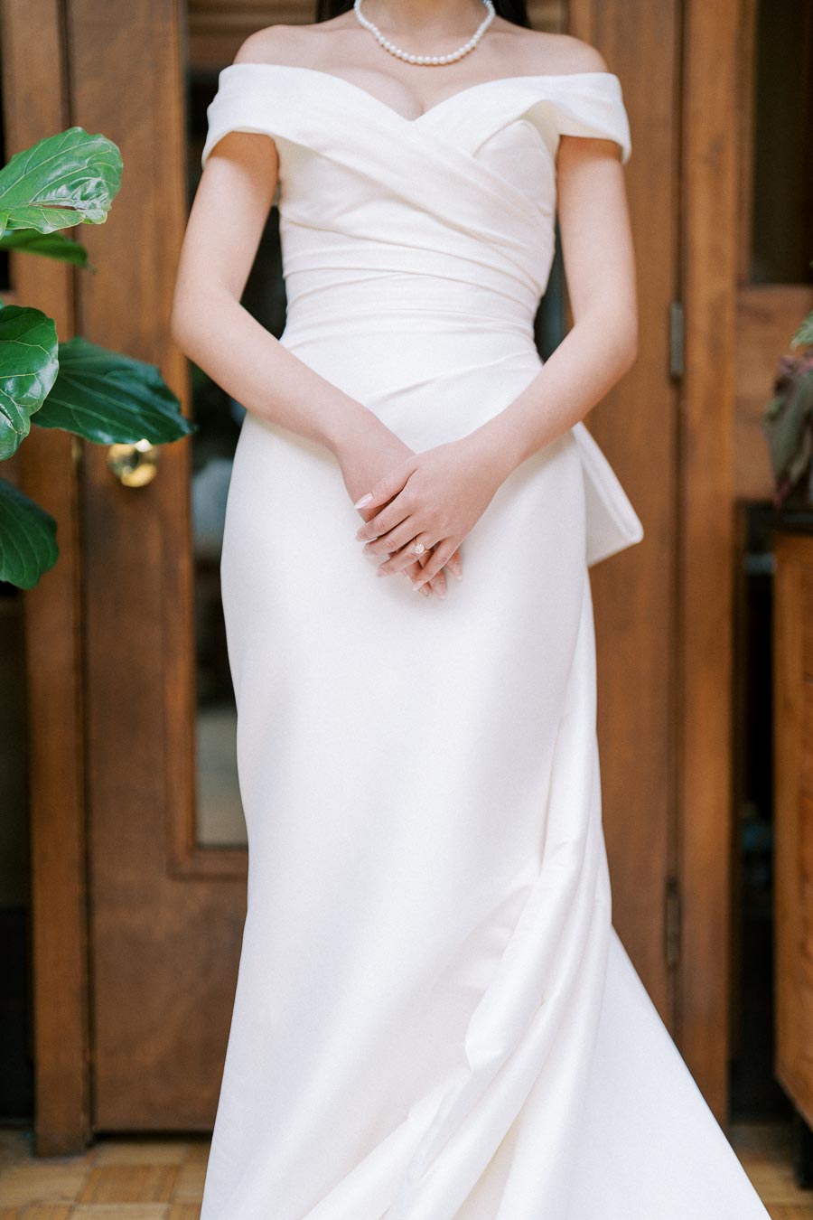 Elegant bride in an off-shoulder white wedding gown, showcasing a modern and sophisticated wedding style, standing in a wooden doorway.