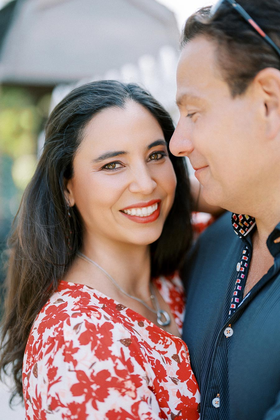 Smiling woman in a red floral dress with a man outdoors, showcasing a cheerful moment.