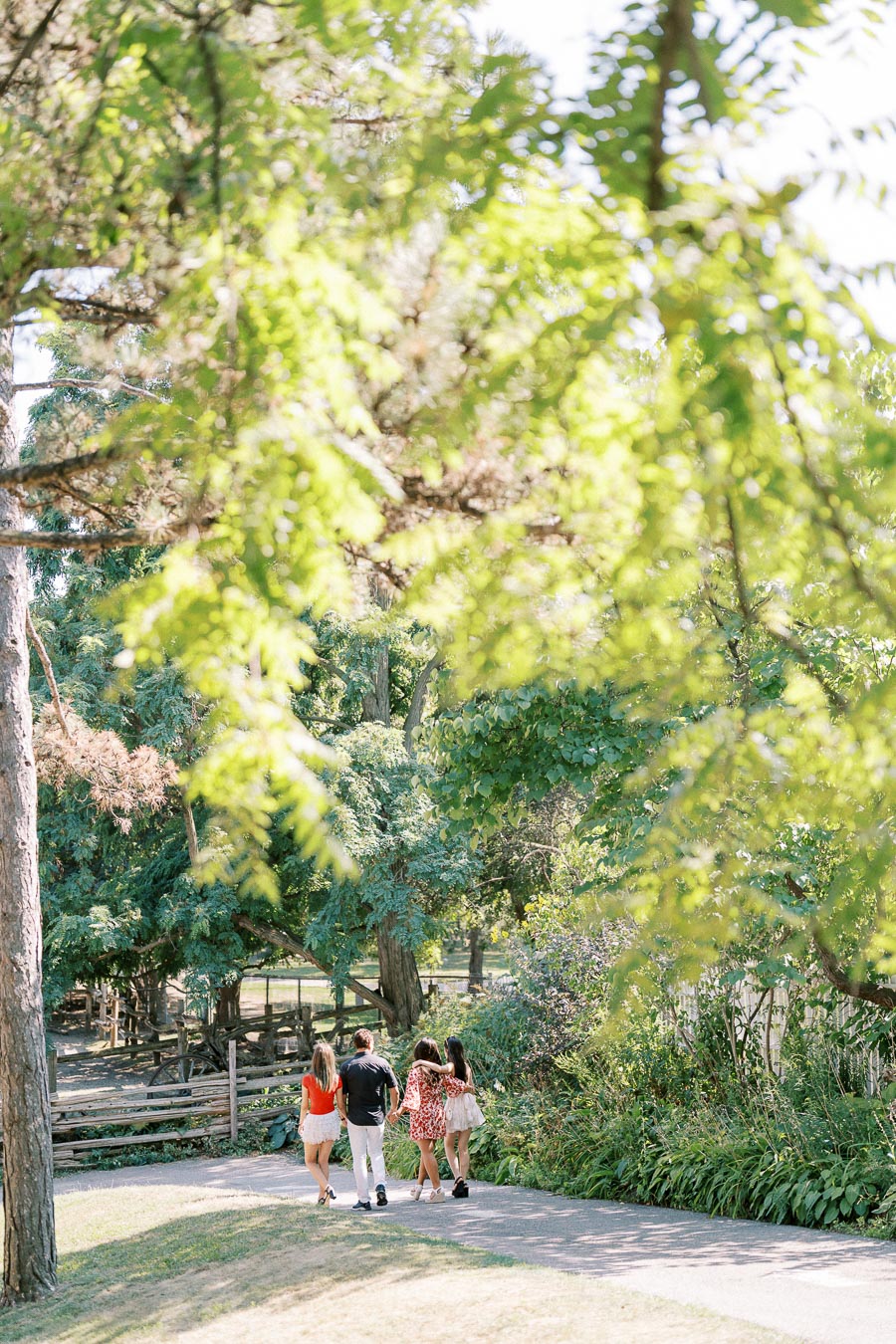Group of friends walking through a lush green park on a sunny day, surrounded by vibrant trees and foliage.