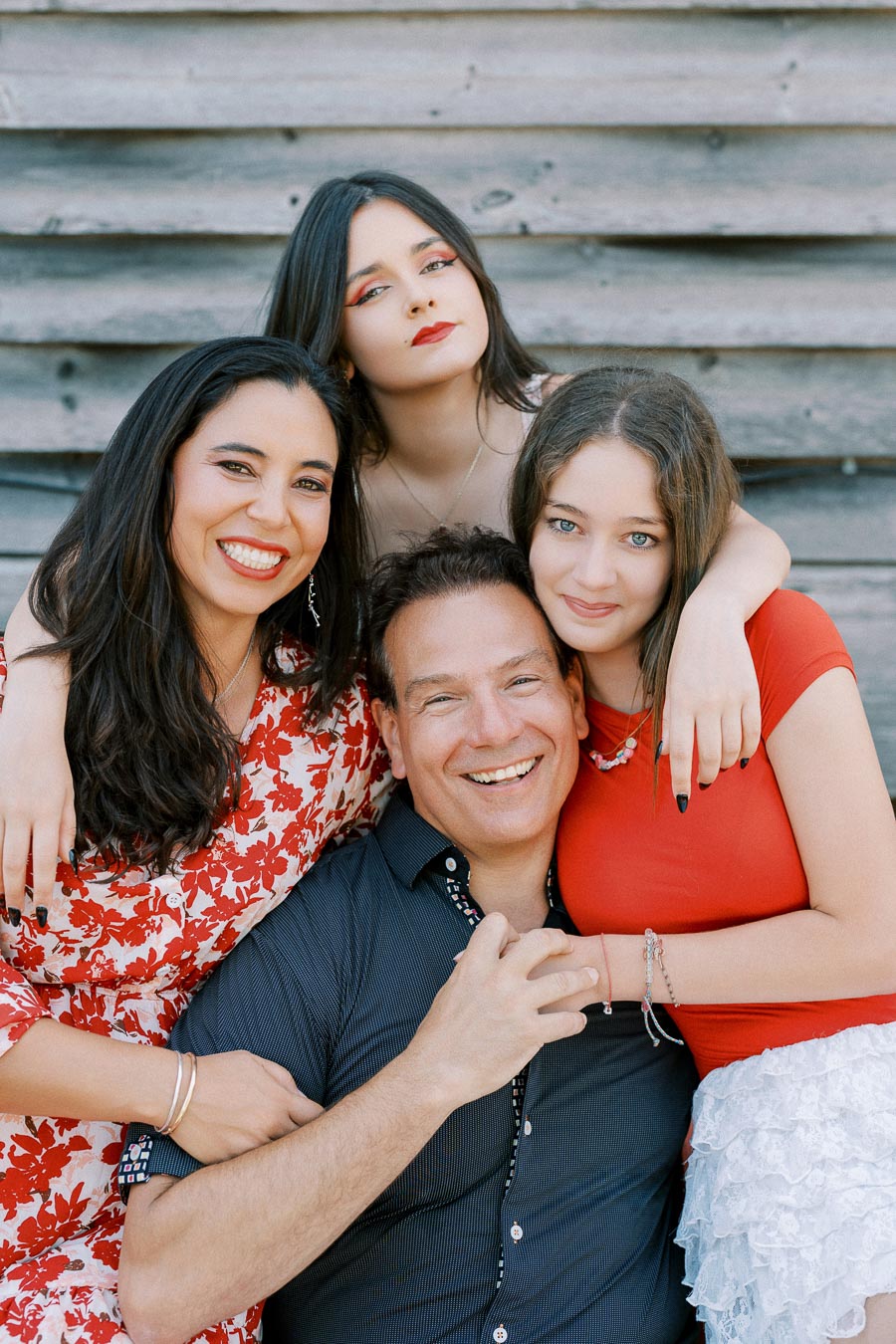 Family portrait of four smiling people in casual attire, with a rustic wooden background.