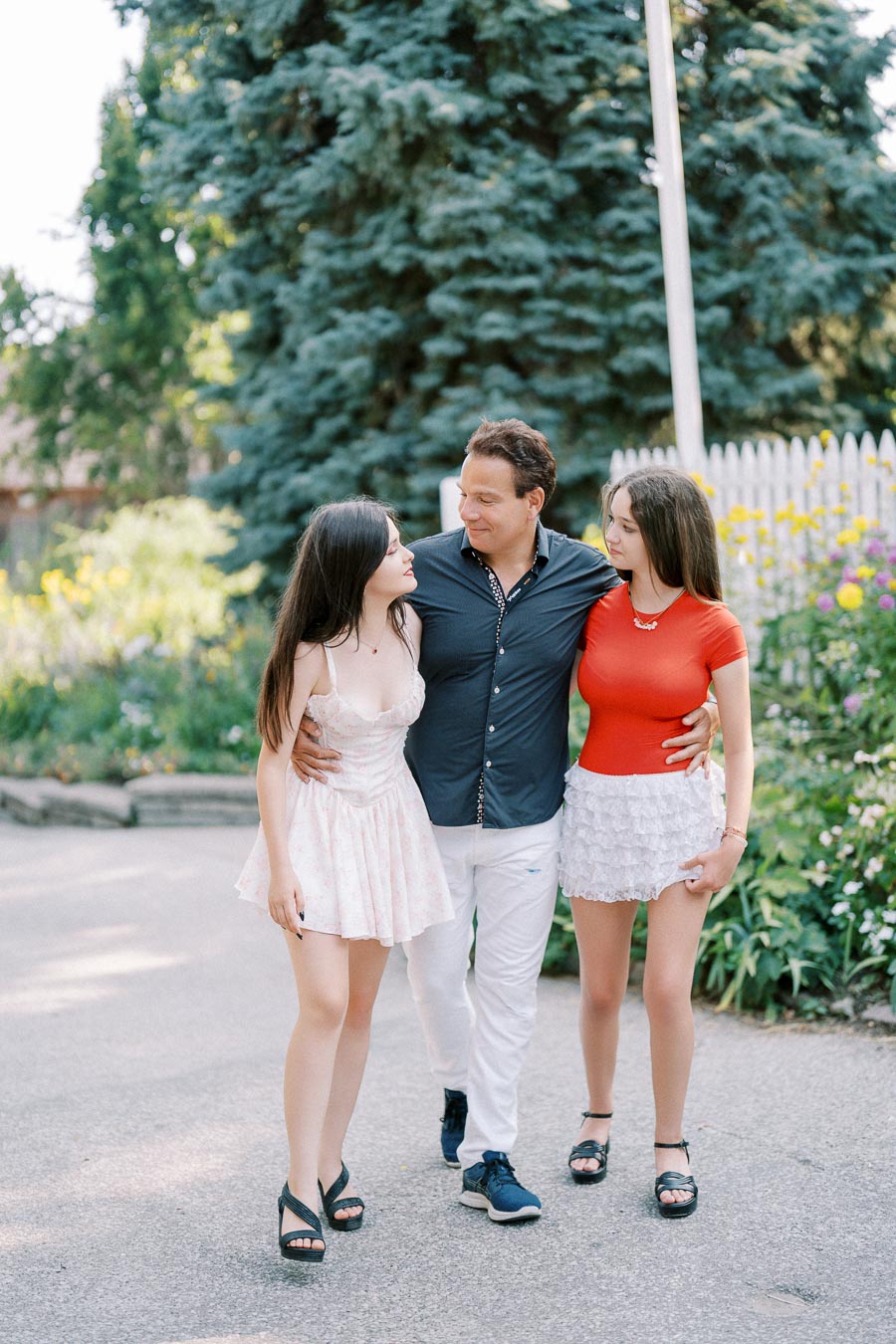 A man walking with two young women in a garden, surrounded by greenery and flowers.