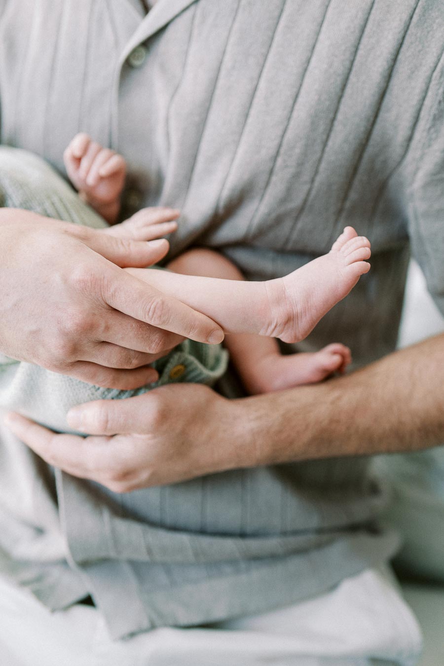 A caring parent gently cradles their newborn’s small foot, highlighting a nurturing bond in a soft-focus setting.