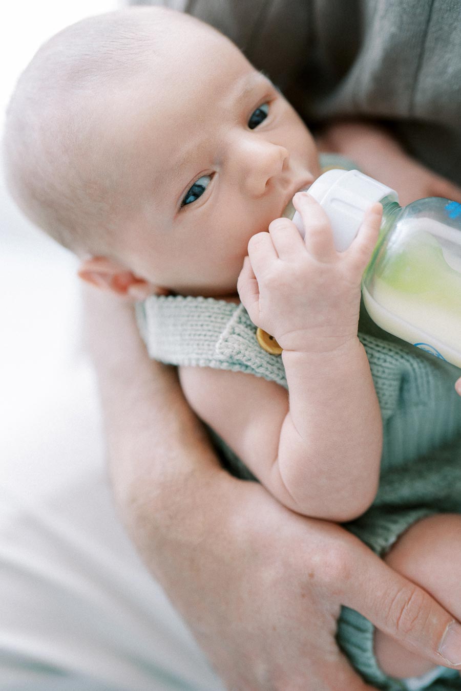 A baby in a knitted outfit being held while drinking from a milk bottle.