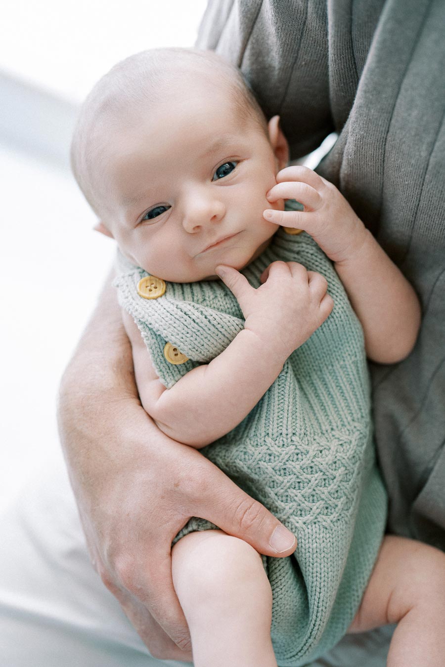 A close-up of a small baby wearing a knitted outfit with buttons being gently cradled, showcasing tenderness and care.