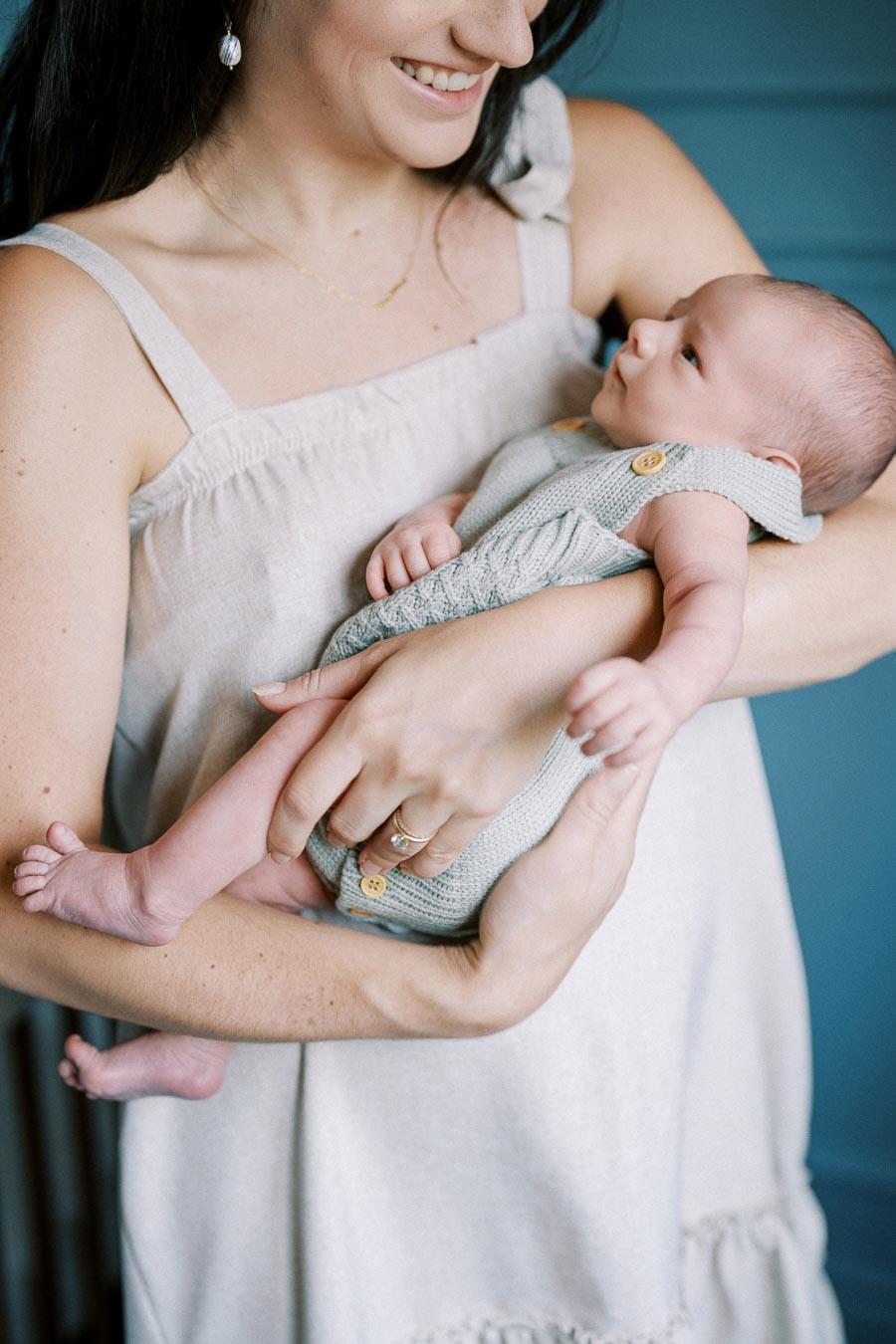 A mother lovingly cradling her newborn baby, both dressed in soft, neutral-toned clothing, with a blue background.
