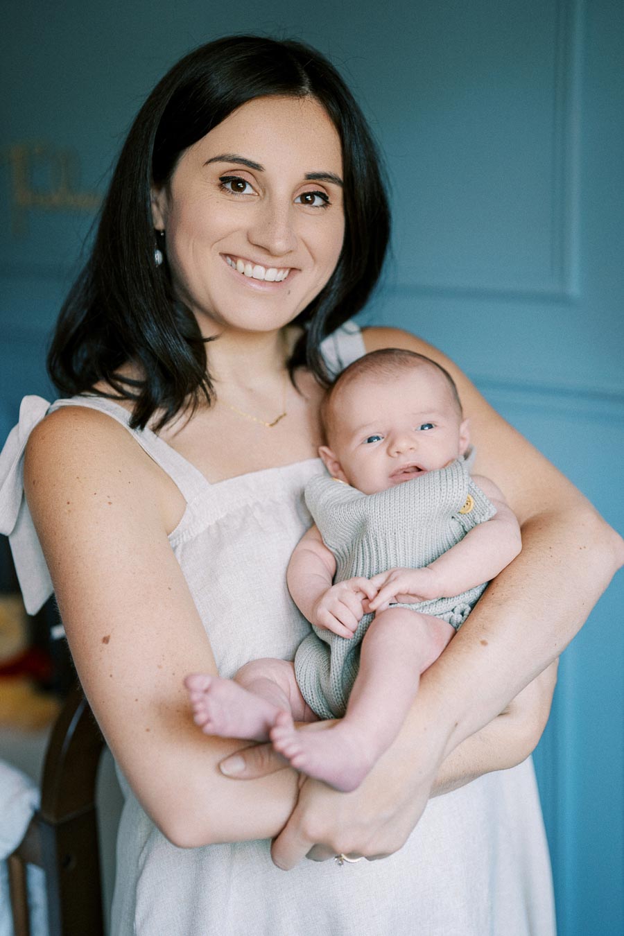 Mother holding baby in arms, both smiling, with blue background, family, parenting, and bonding concept.