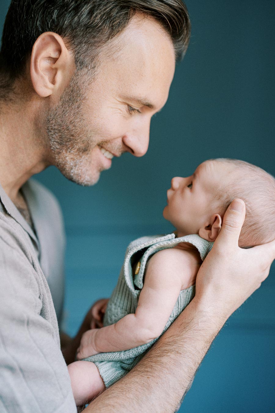 Father lovingly holding and gazing at his newborn baby, capturing a tender moment of parenthood against a soft blue background.