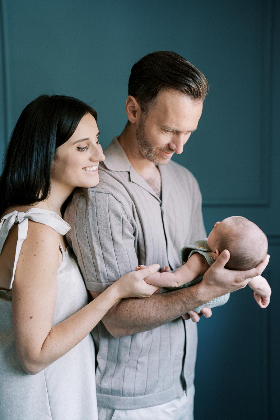 Happy couple holding their newborn baby against a teal background, showcasing family love and togetherness.
