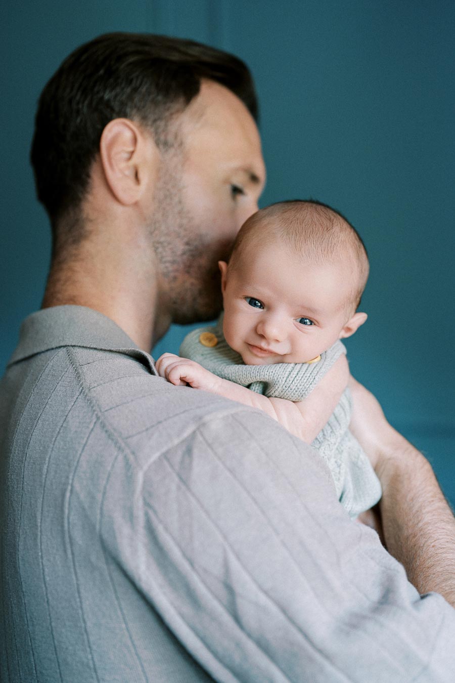 Father holding smiling baby on shoulder against a blue background, showcasing family bonding and tenderness.