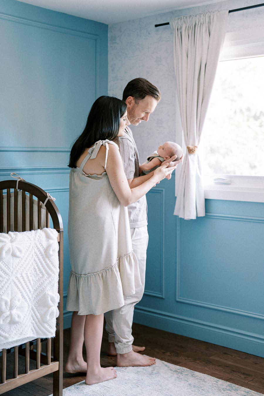 Couple bonding with their newborn in a blue nursery, capturing a tender family moment.