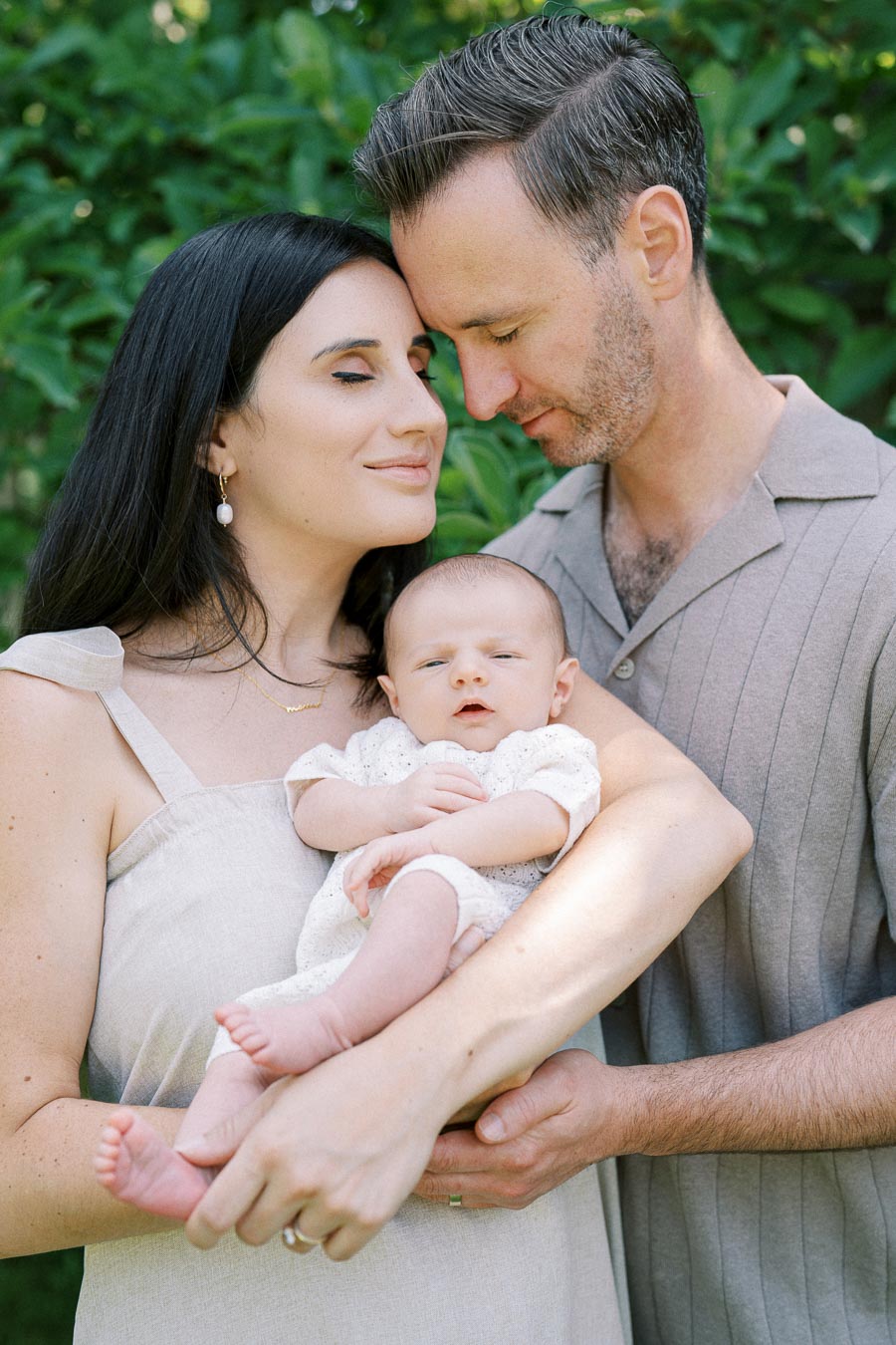 A loving couple gently holding their newborn baby outdoors, surrounded by lush green foliage, capturing a serene family moment.