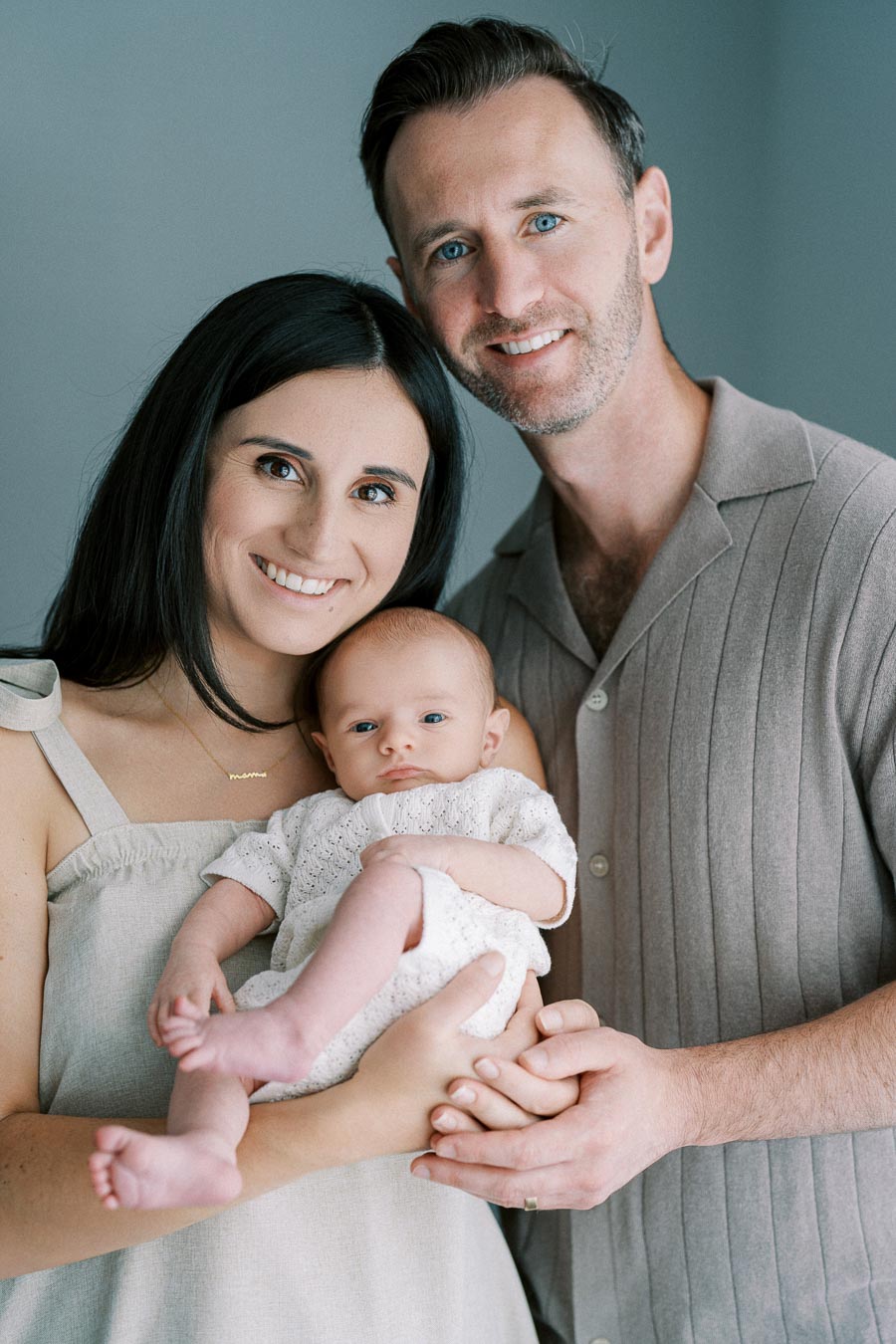 Smiling couple holding their baby, capturing a joyful family moment in a softly lit room.