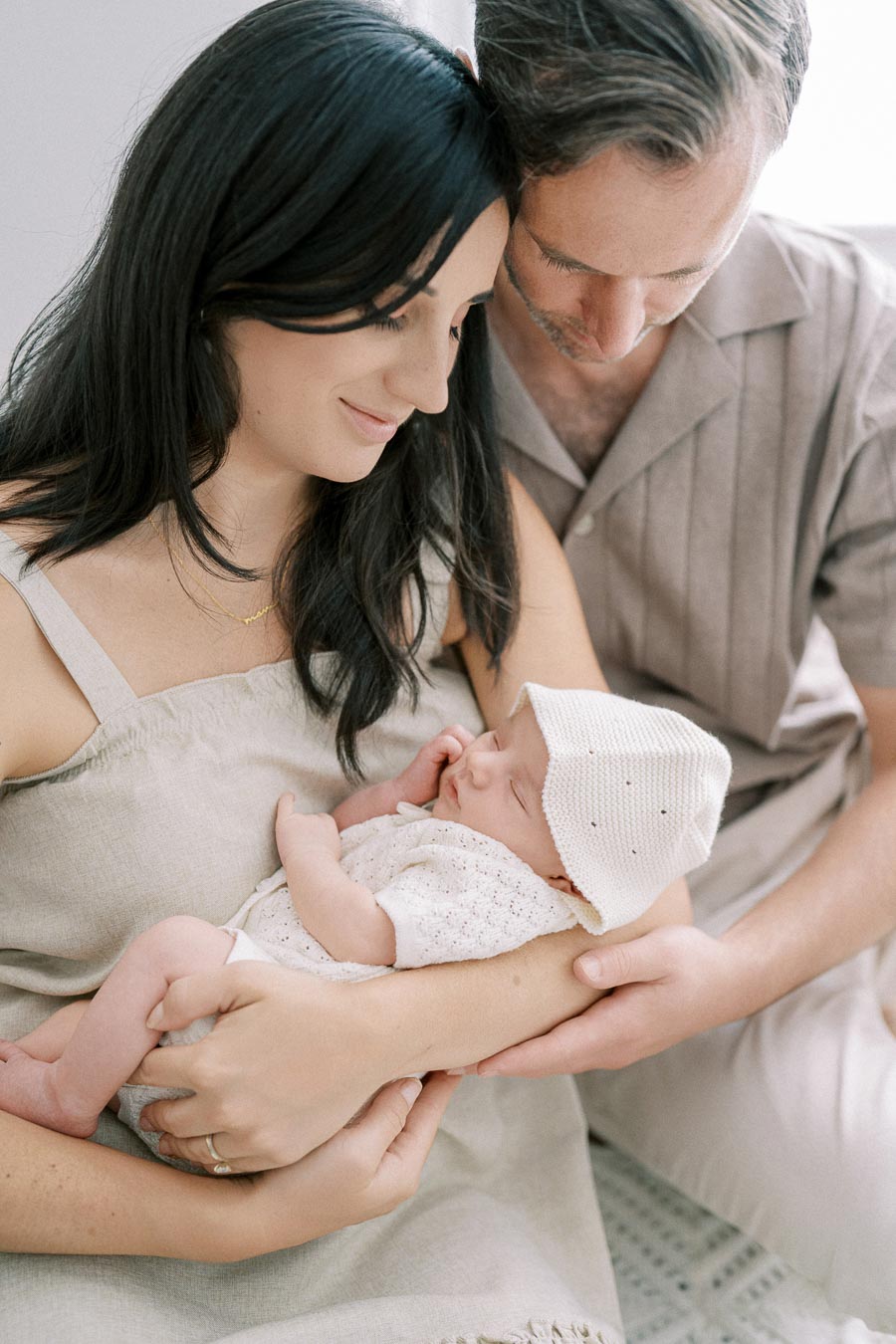 A loving couple gently cradles their sleeping newborn baby, showcasing a tender family moment.
