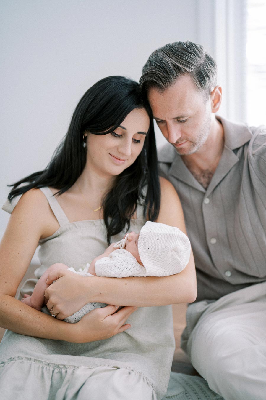 Family portrait featuring a loving couple gently cradling their newborn baby, highlighting the warmth and tenderness of parenthood in a serene home setting.