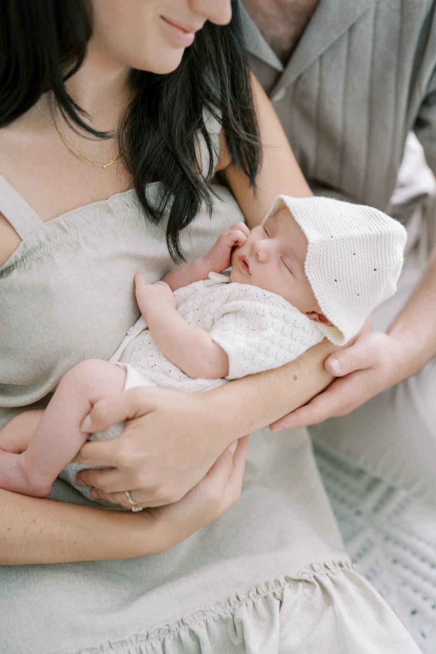 A mother gently cradling her sleeping newborn baby, dressed in a white knit outfit and hat, highlighting a tender family moment.