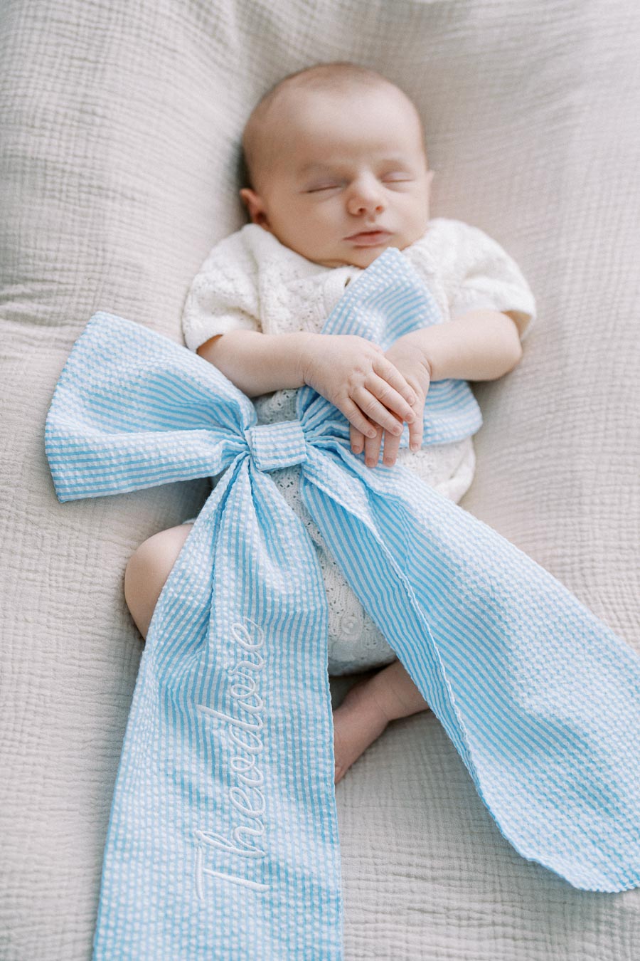 A sleeping baby wrapped in a blue-striped blanket with a large bow, lying on a soft, textured surface.