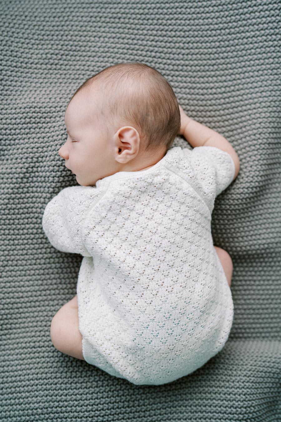 Sleeping newborn baby in white knitted outfit during in-home Toronto lifestyle session