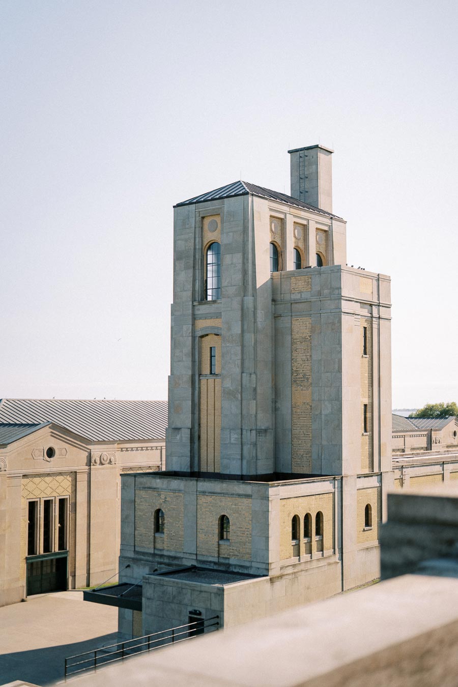 Historic stone building with arched windows and a tall tower against a clear blue sky.