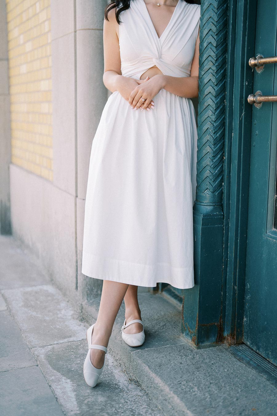 Elegant woman in white summer dress standing against a teal doorway, showcasing a chic and timeless fashion style.