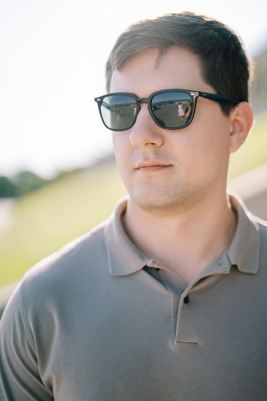 Man wearing sunglasses and a gray polo shirt outdoors on a sunny day.