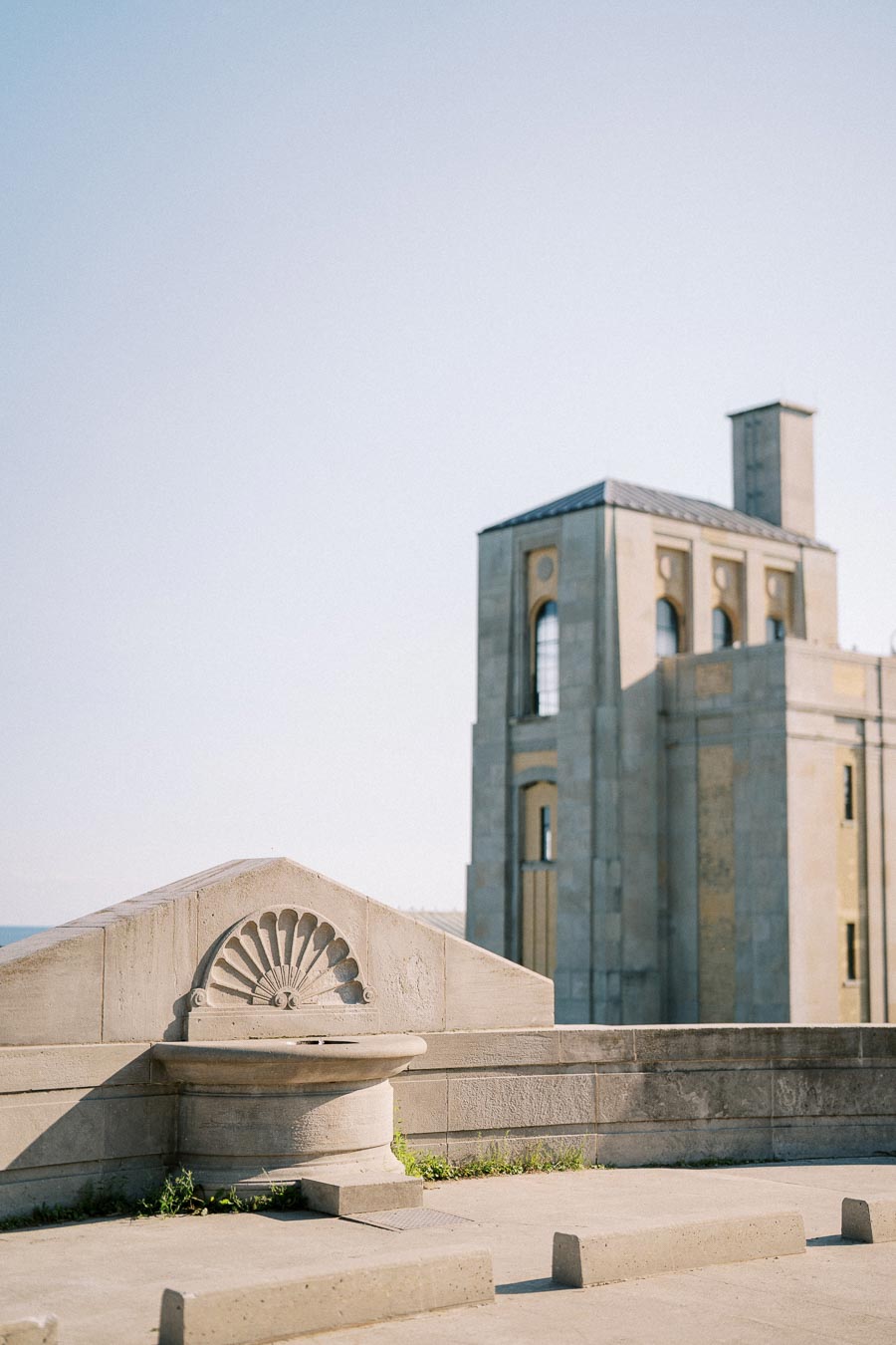 Historic stone architecture featuring a decorative wall detail and a tall building with arched windows, set against a clear blue sky.