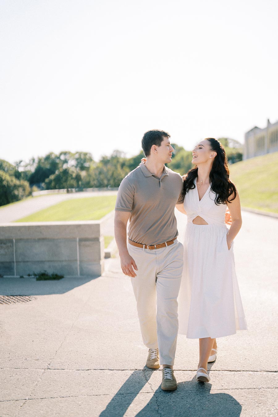 Happy couple walking outdoors on a sunny day, wearing casual summer attire, with a bright green landscape and clear sky in the background.