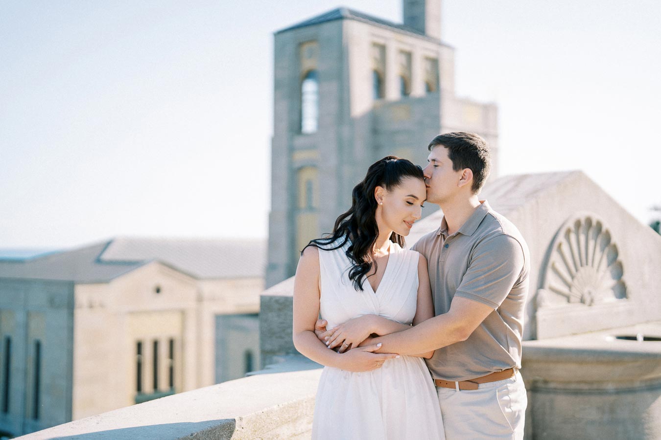 A couple embracing on a sunlit balcony with historic architecture in the background, capturing a romantic moment.