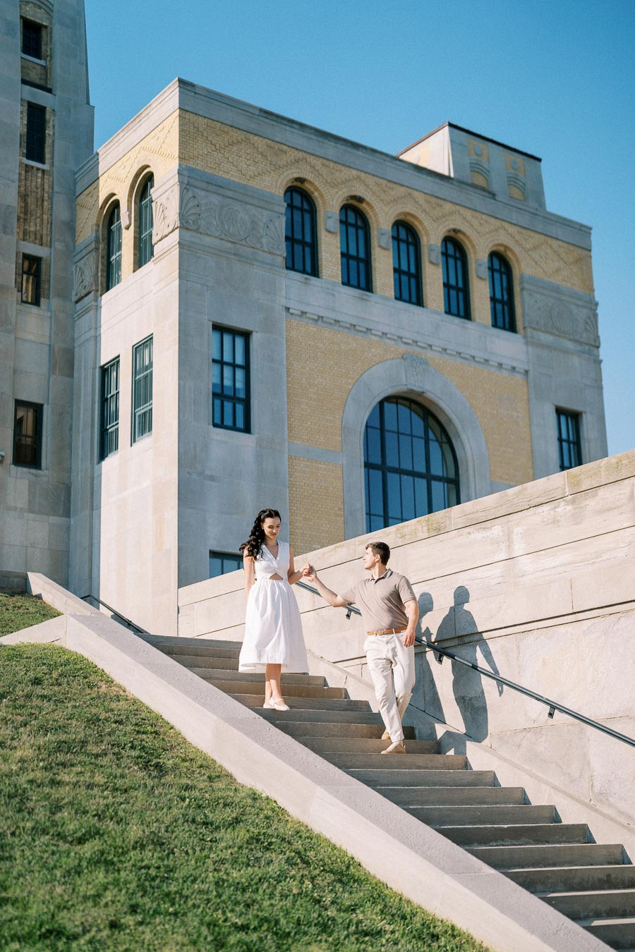Couple walking down stairs of a historic building, enjoying a sunny day with clear blue skies.