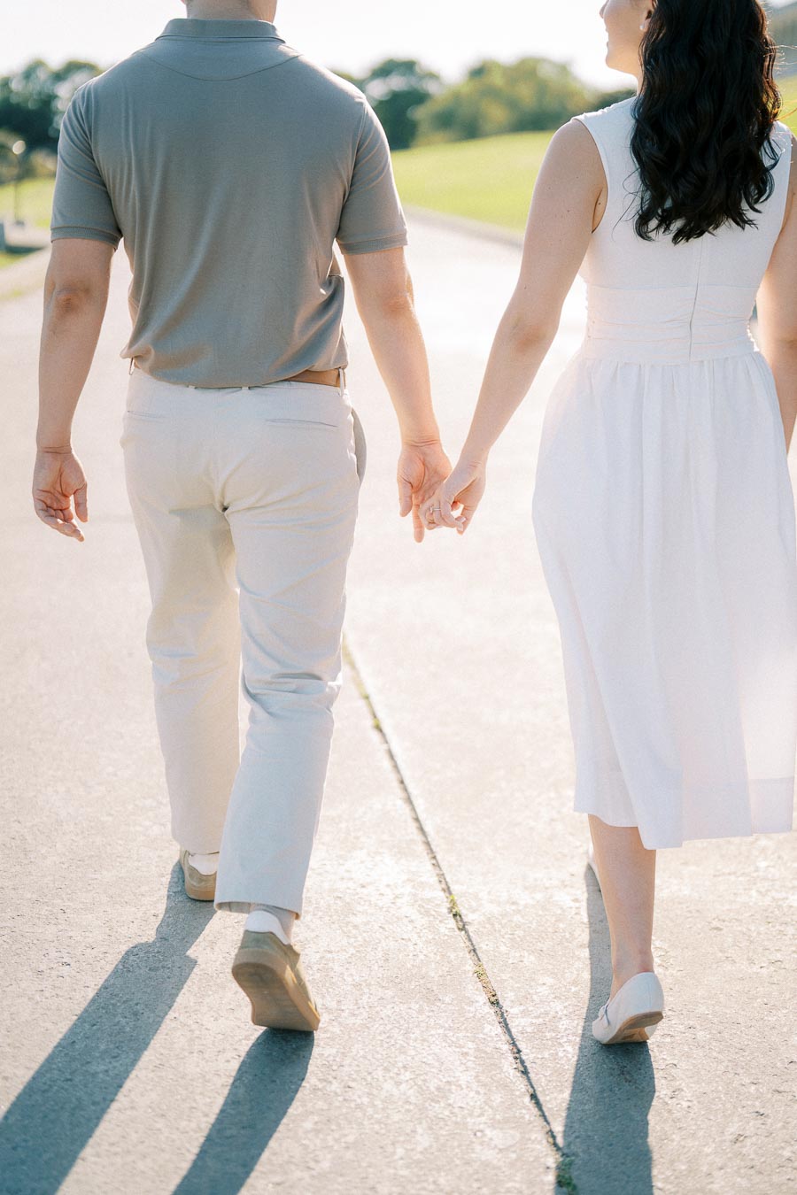 A couple walking hand in hand on a sunny day, dressed in light summer clothing, symbolizing love and togetherness.