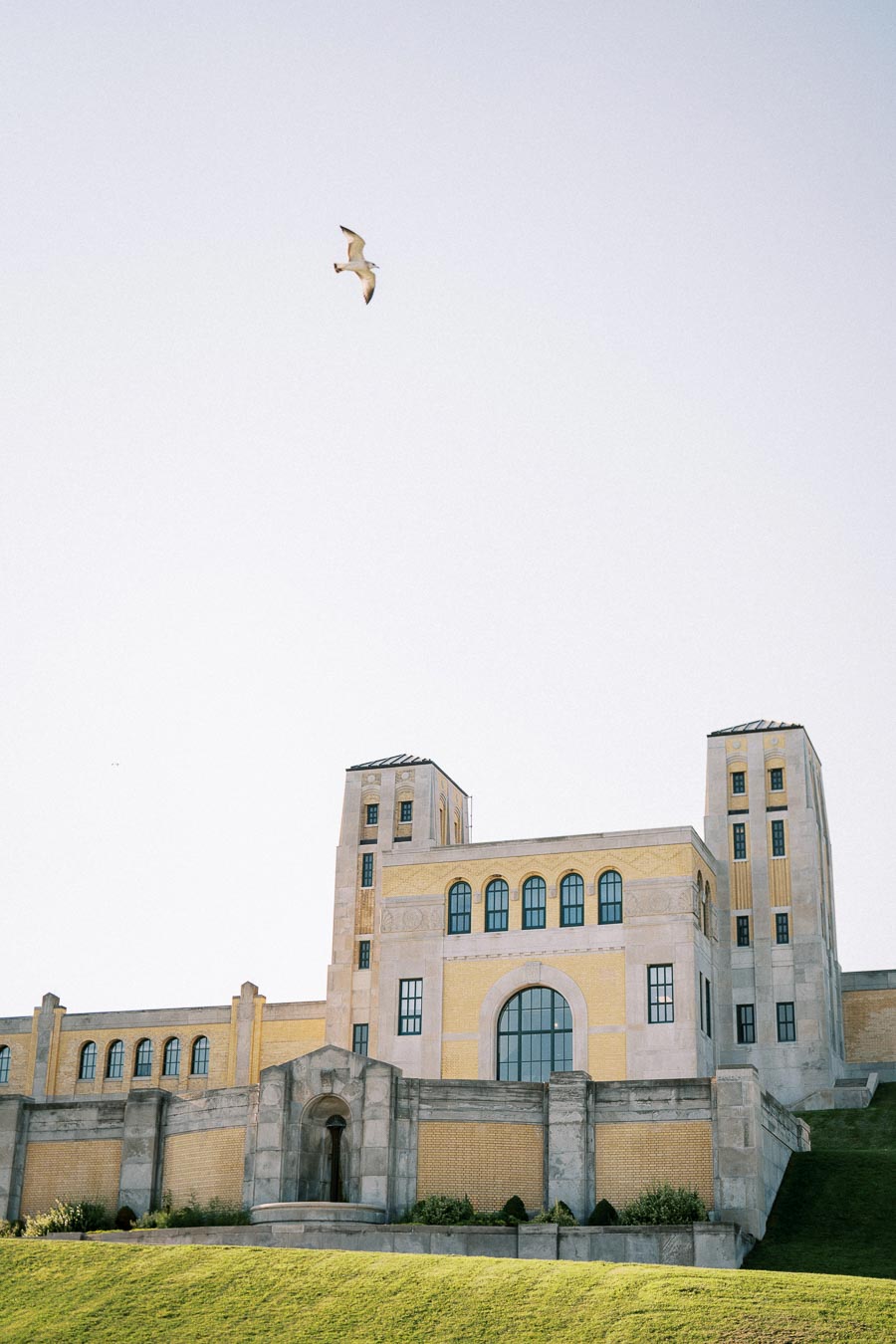 Historic building with towers under clear sky, featuring a seagull flying above, set against a grassy foreground.