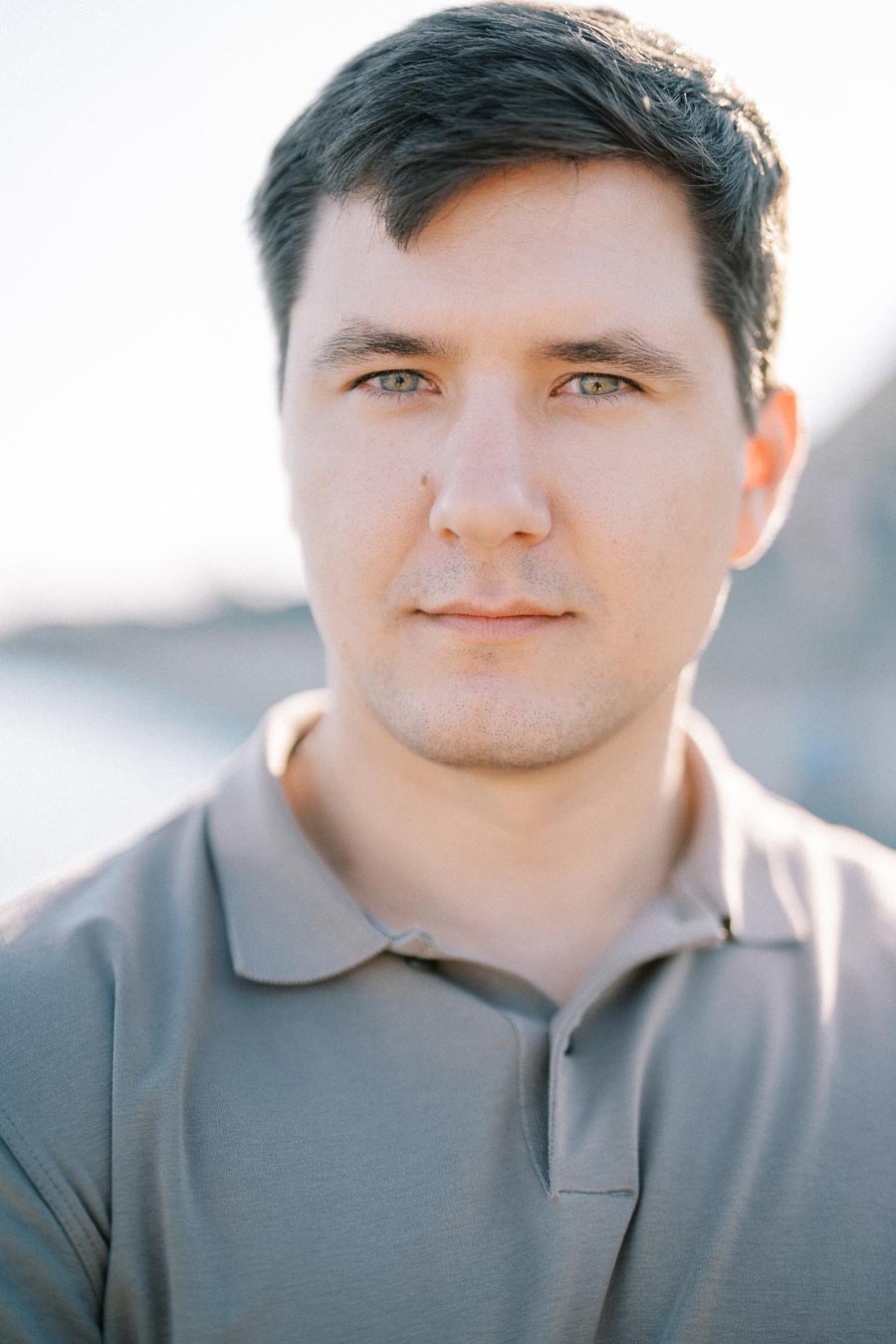 Portrait of a man in a grey polo shirt with a blurred outdoor background, looking directly at the camera.