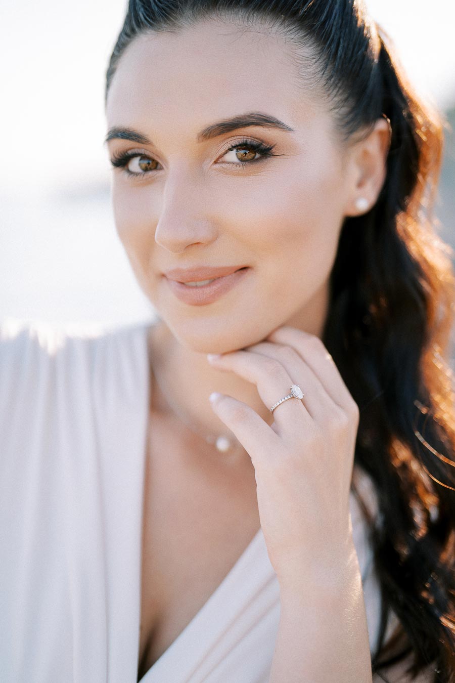 Portrait of a woman with long dark hair, wearing a diamond engagement ring, showcasing natural beauty and elegance.