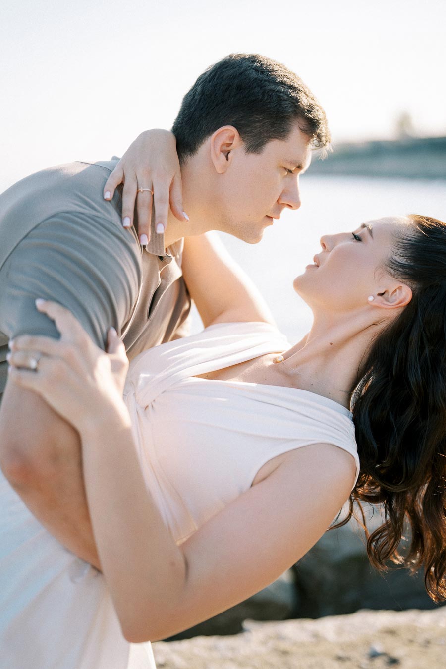 Romantic couple embracing by the waterfront, sharing an intimate moment on a sunny day.