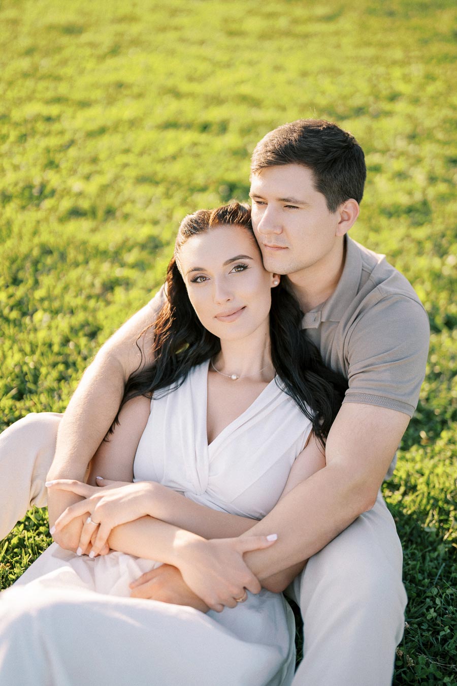 A couple sitting on grass, embracing each other lovingly as they enjoy a sunny day outdoors.
