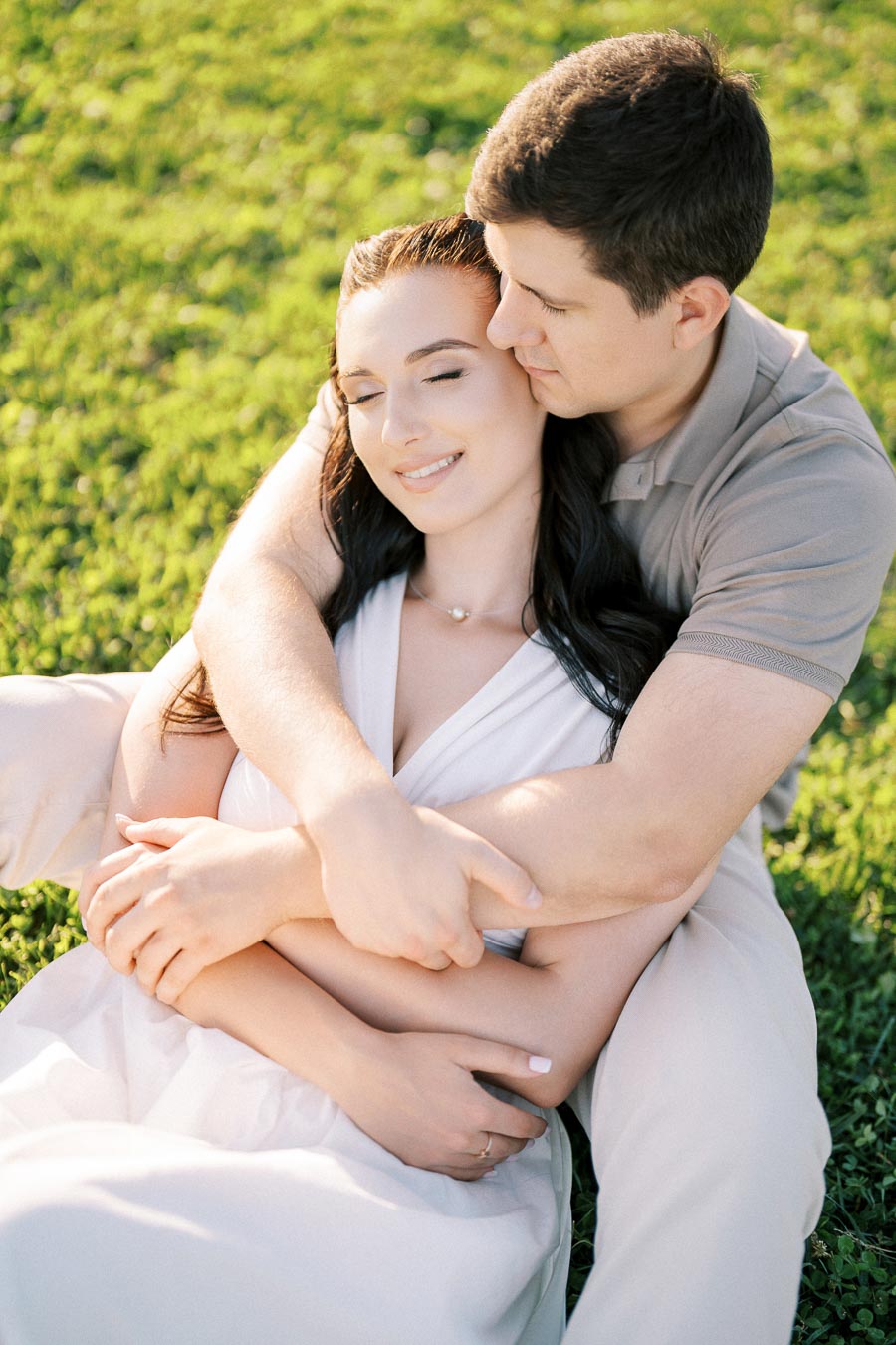 Romantic couple embracing on a grassy field during sunset, showcasing love and closeness in a serene outdoor setting.