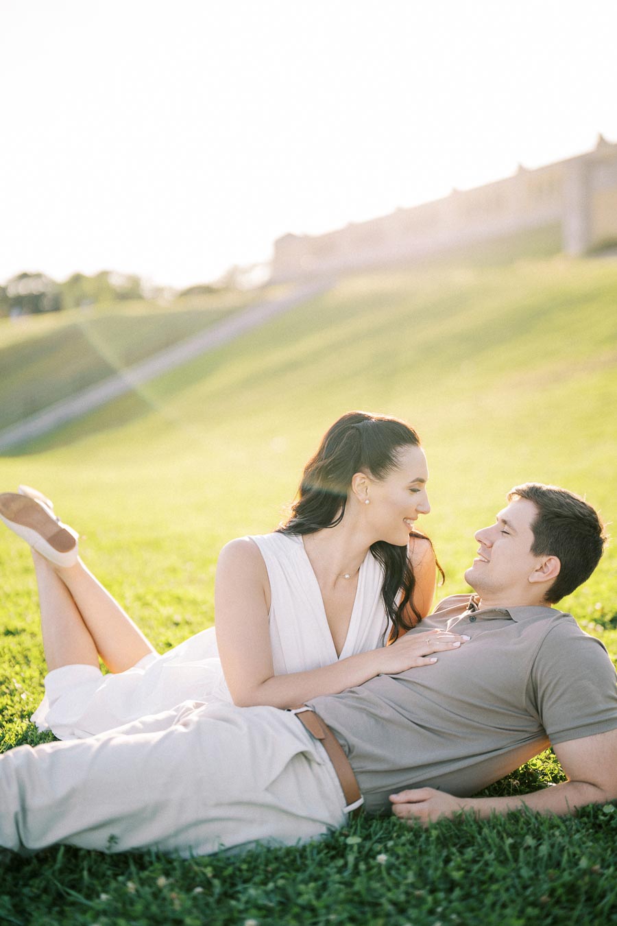 Couple enjoying a sunny day lounging on a grassy hill, with warm sunlight creating a romantic atmosphere.