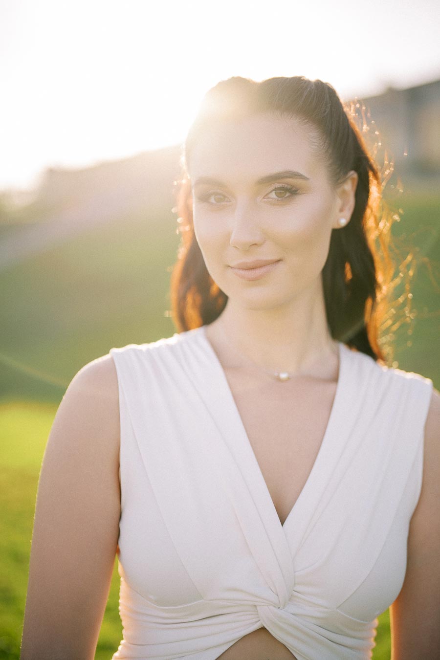 Young woman in a white dress standing outdoors with sunlight shining behind her.