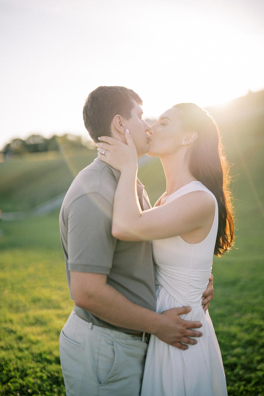 A couple sharing a romantic kiss in a sunlit park, surrounded by lush green grass.