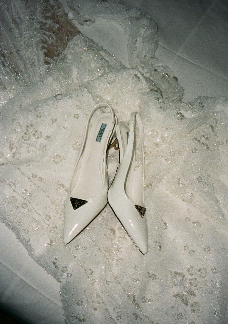 Elegant white high-heeled shoes with designer logo placed on a detailed, beaded lace fabric background.