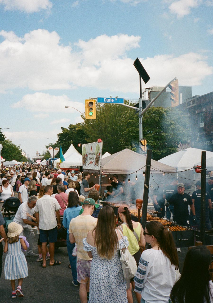 Crowded street festival with people enjoying food stalls and outdoor vendors under a blue sky on Durie Street.
