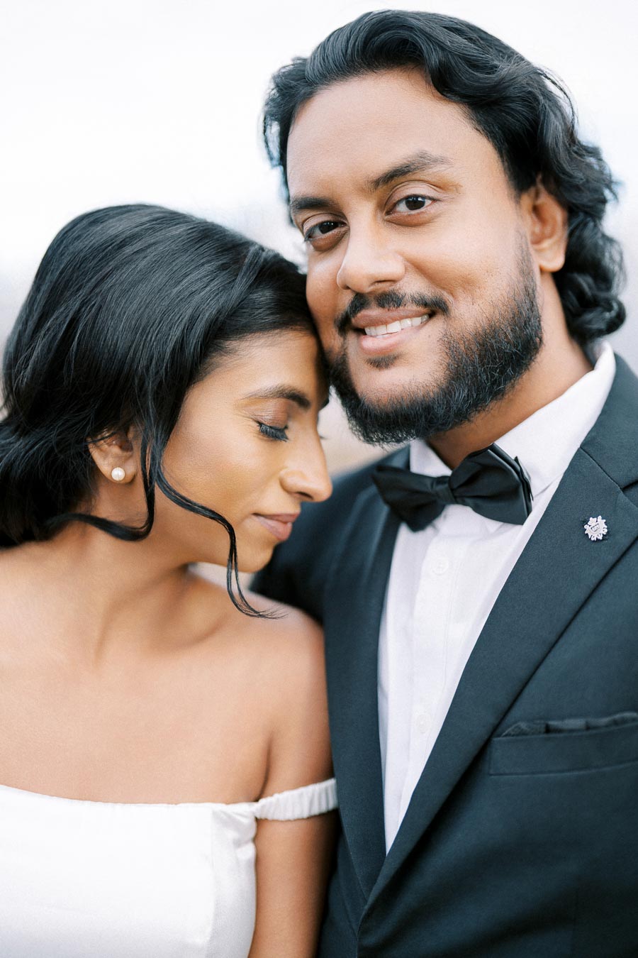 Happy couple embracing on their wedding day, with the woman wearing an off-shoulder gown and the man in a suit with a bow tie, showing affection and joy.