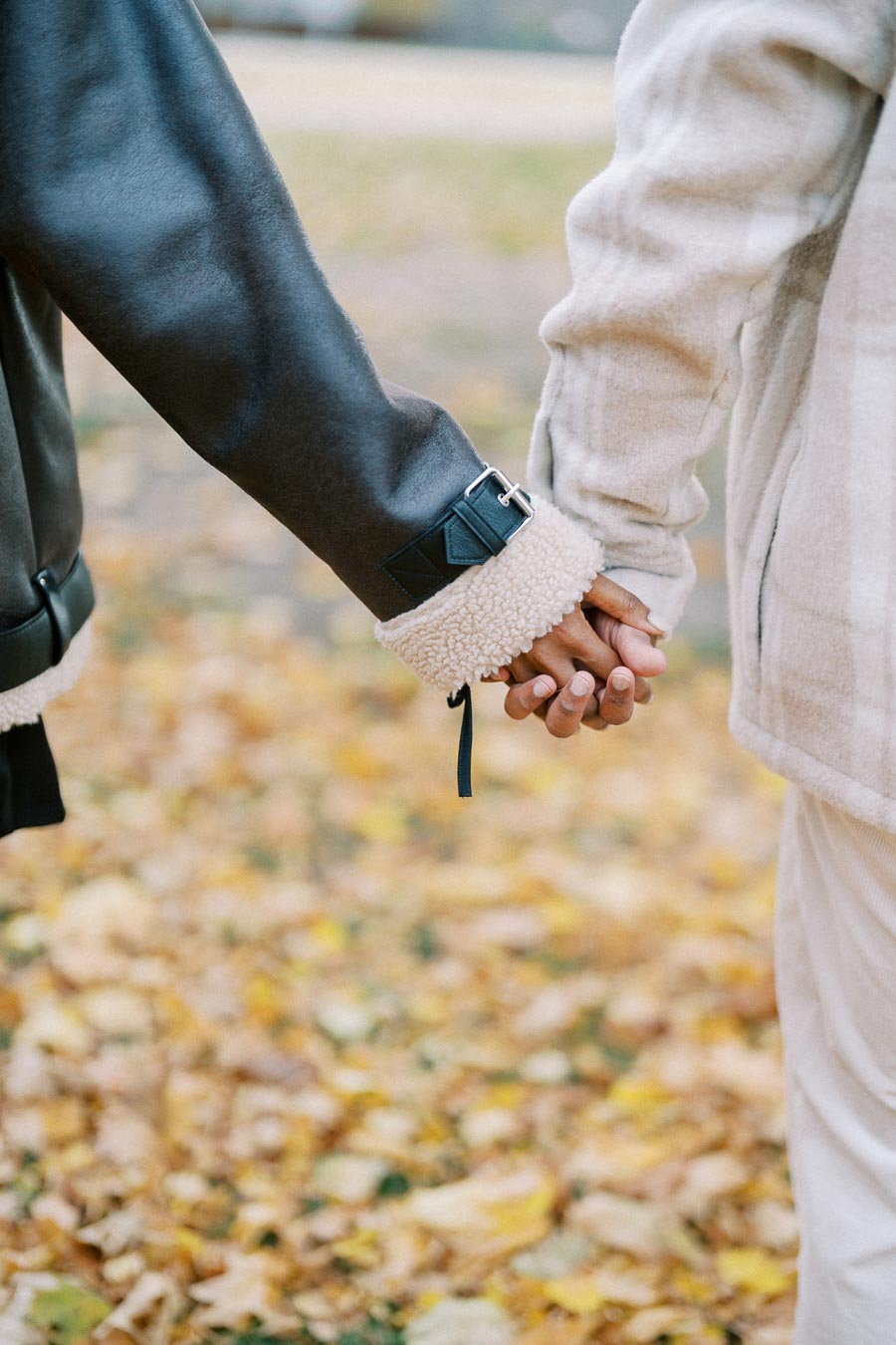 Two people holding hands in cozy autumn jackets, surrounded by fallen leaves.