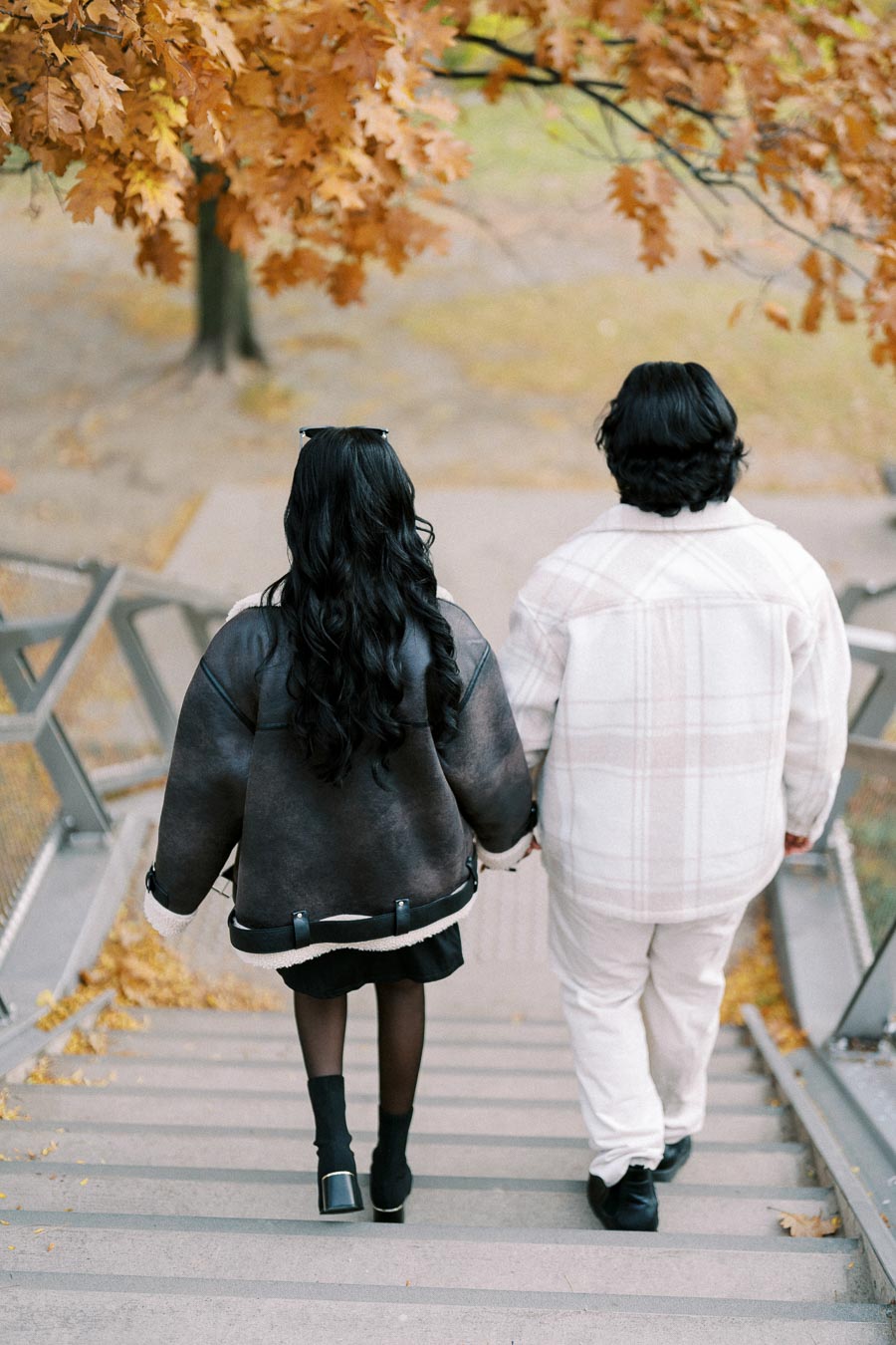 Couple walking down a staircase in autumn, surrounded by orange and brown leaves, wearing stylish jackets.