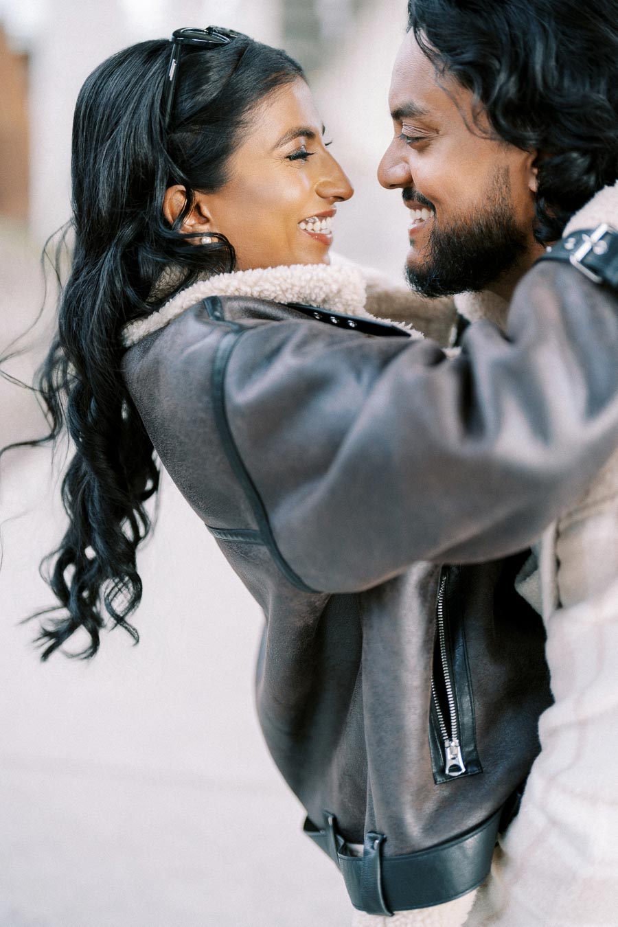 A couple smiling and embracing each other while wearing cozy jackets outdoors.