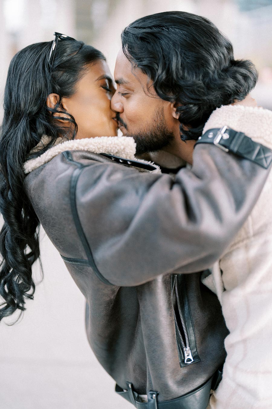A romantic couple sharing a kiss while embracing, both wearing cozy winter jackets, showcasing love and warmth in a candid moment.